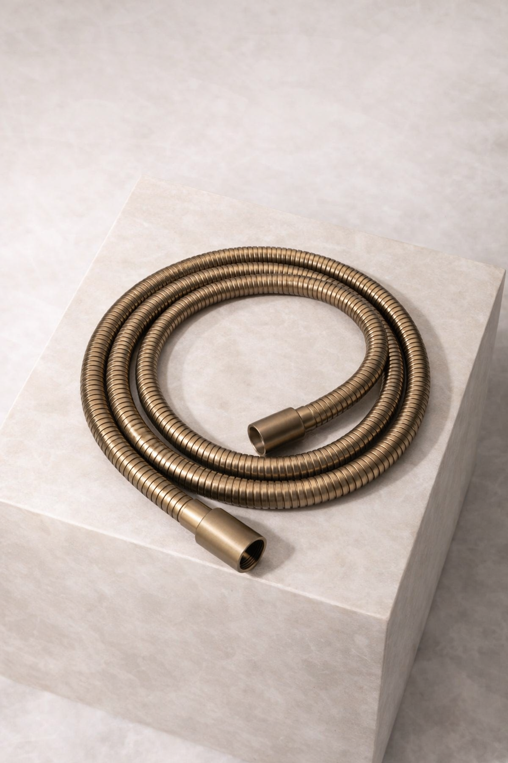 Antique Brass hose coiled on a white pedestal against a light background