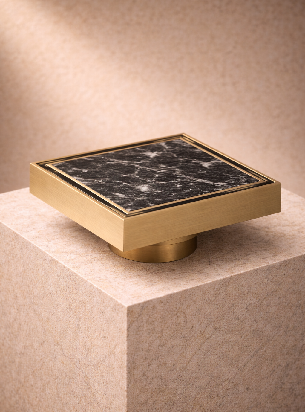 Decorative square floor drain object with an antique brass frame and black marble centre on a beige pedestal.