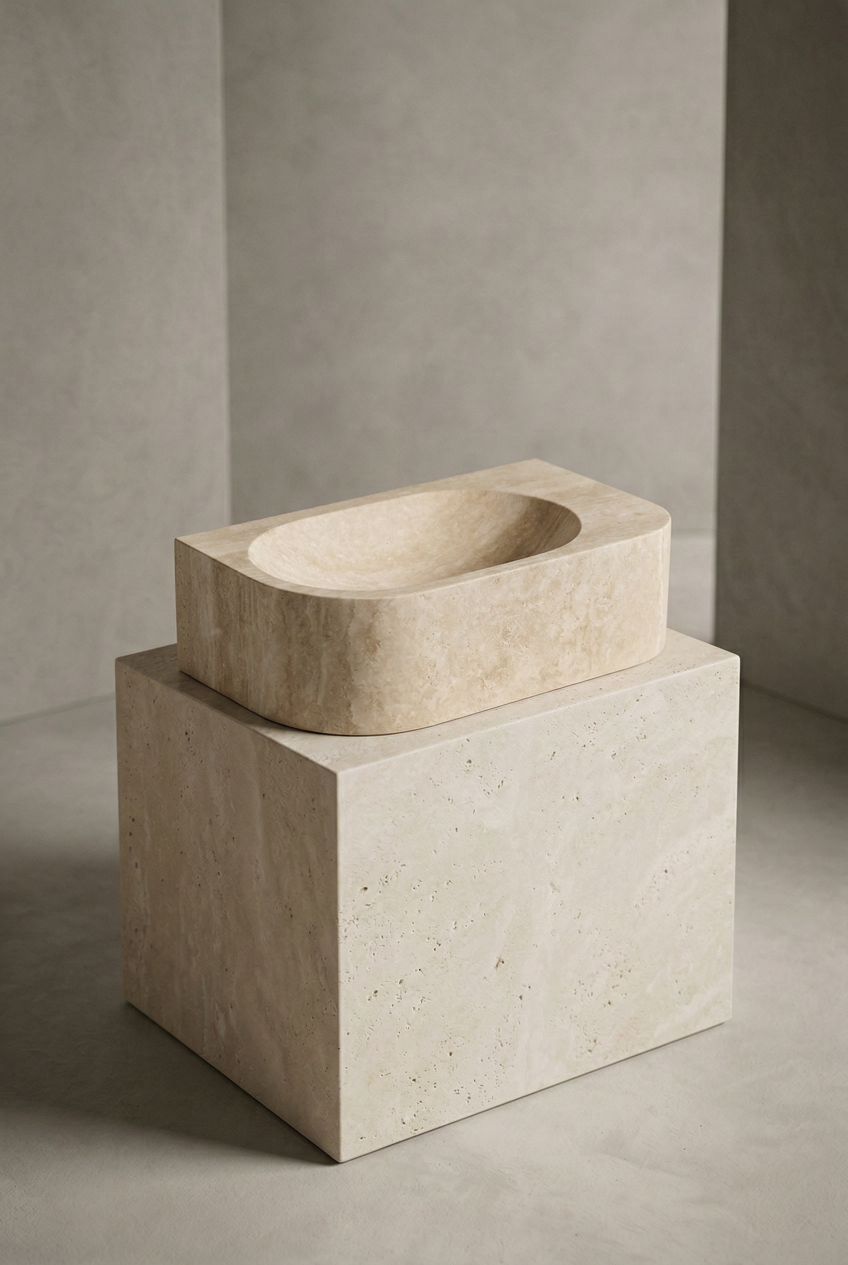 Beige stone sink on a matching pedestal against a neutral wall.