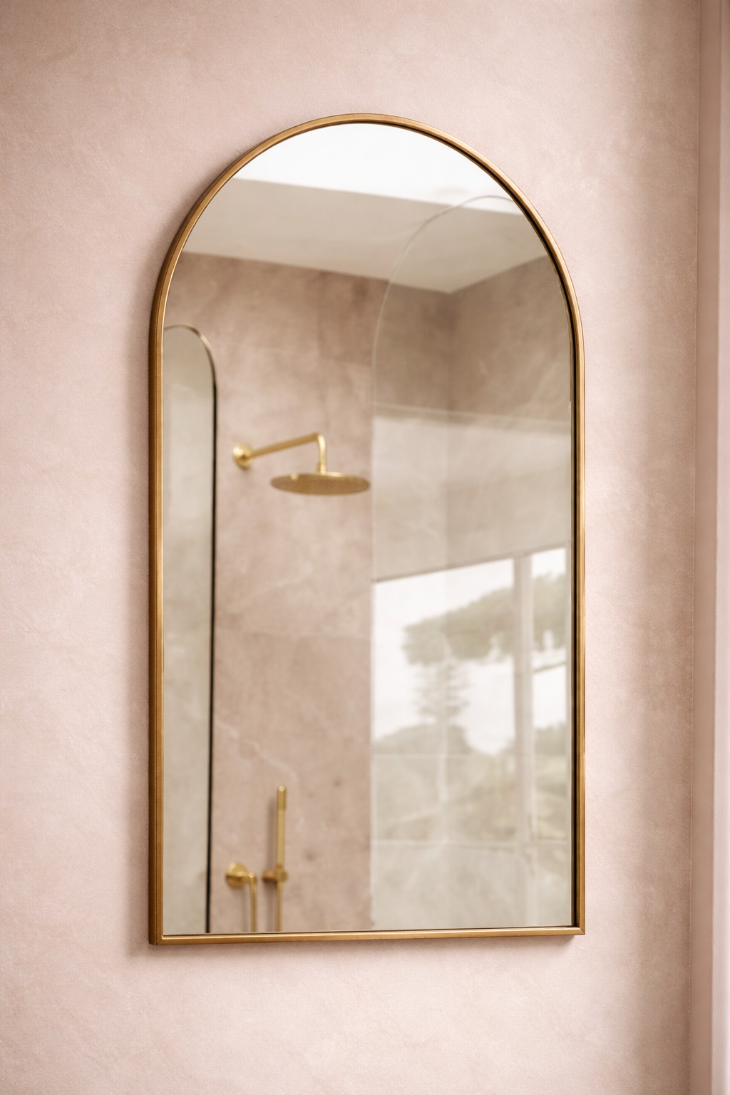 Gold-framed mirror on a light pink wall with bathroom fixtures.